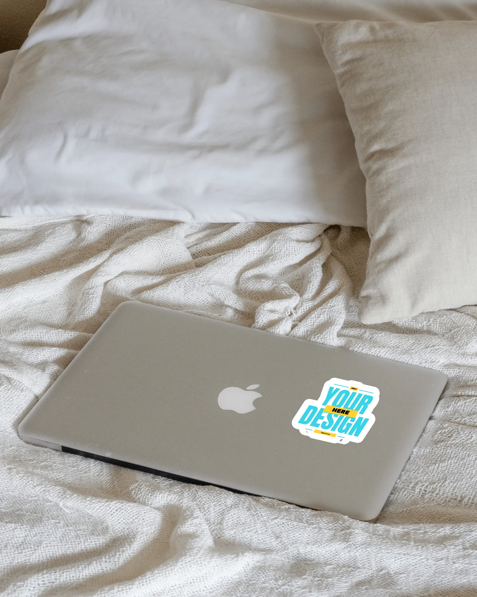 sticker mockup on a macbook lying on a bed