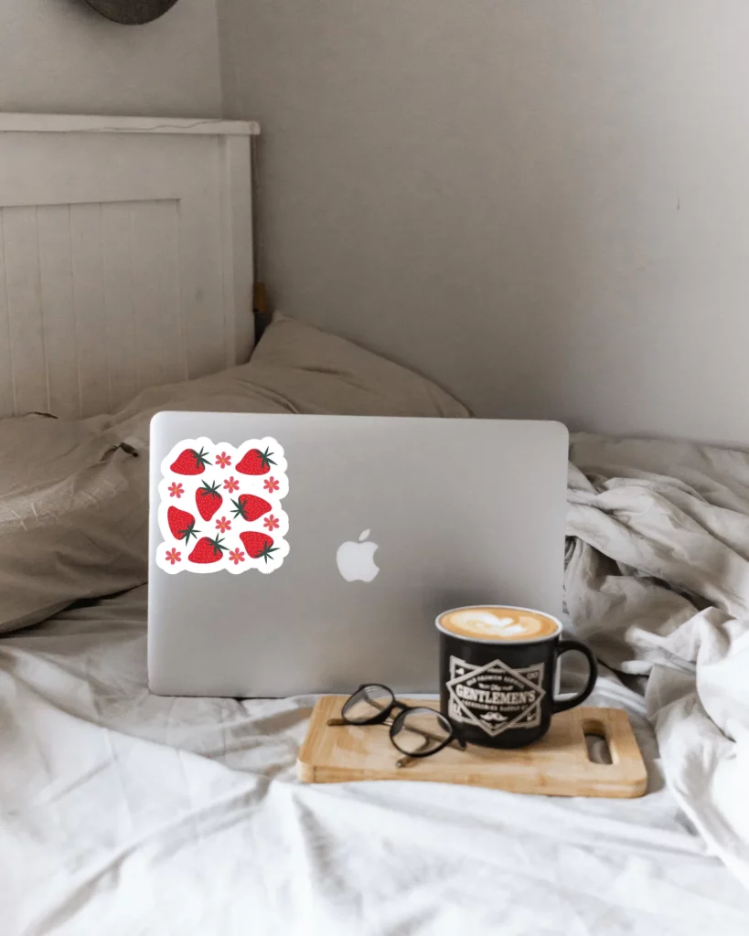 sticker mockup on a macbook with coffee cup and glasses on bed