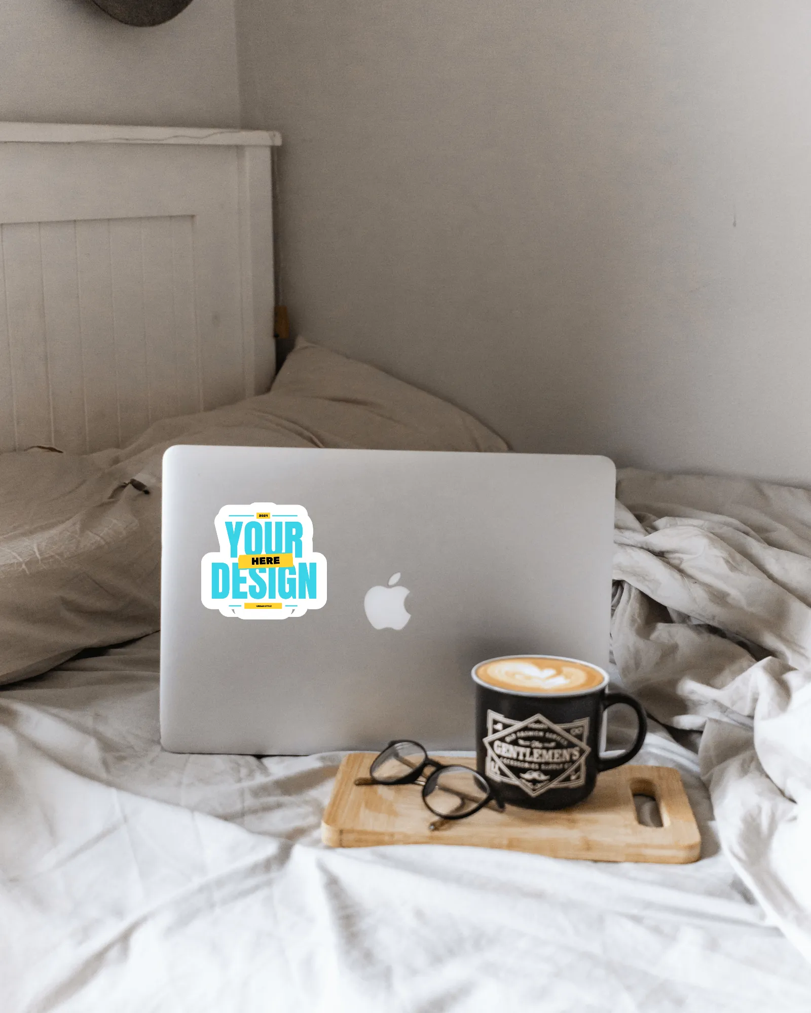 sticker mockup on a macbook with coffee cup and glasses on bed